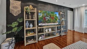 A living room with a black brick wall, wooden shelves, a TV, and a potted plant. - NEW! Spacious Relaxing Home With  Boat Dock (Hollywood)