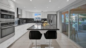 A modern kitchen with white cabinets, stainless steel appliances, a granite countertop, and two black bar stools. - NEW! Spacious Relaxing Home With  Boat Dock (Hollywood)