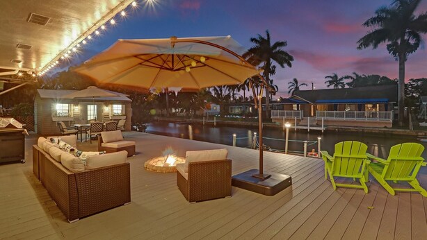 A deck with wicker furniture, a fire pit, and a view of a body of water at dusk. - NEW! Spacious Relaxing Home With  Boat Dock (Hollywood)