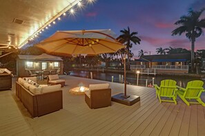 A deck with wicker furniture, a fire pit, and a view of a body of water at dusk.