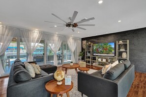 A modern living room with a ceiling fan, a large TV, and a brick accent wall.