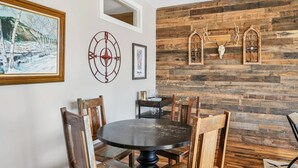 A dining area with a round table and wooden chairs, rustic wooden wall paneling, and mounted deer skulls.