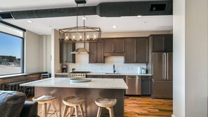 A modern kitchen with a central island, bar stools, and stainless steel appliances.