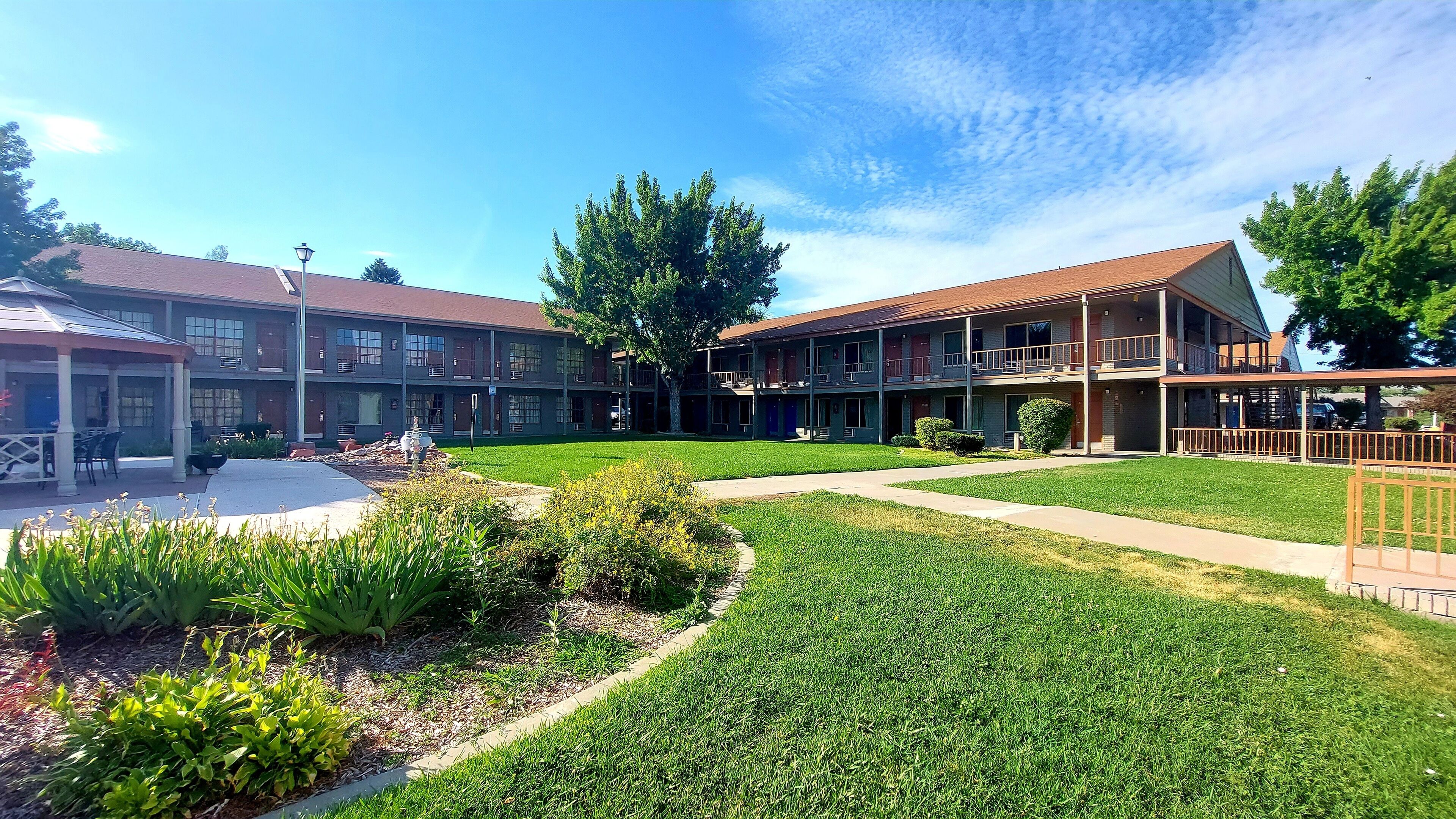 A courtyard with a covered seating area, a building with multiple balconies, and a well-maintained lawn.