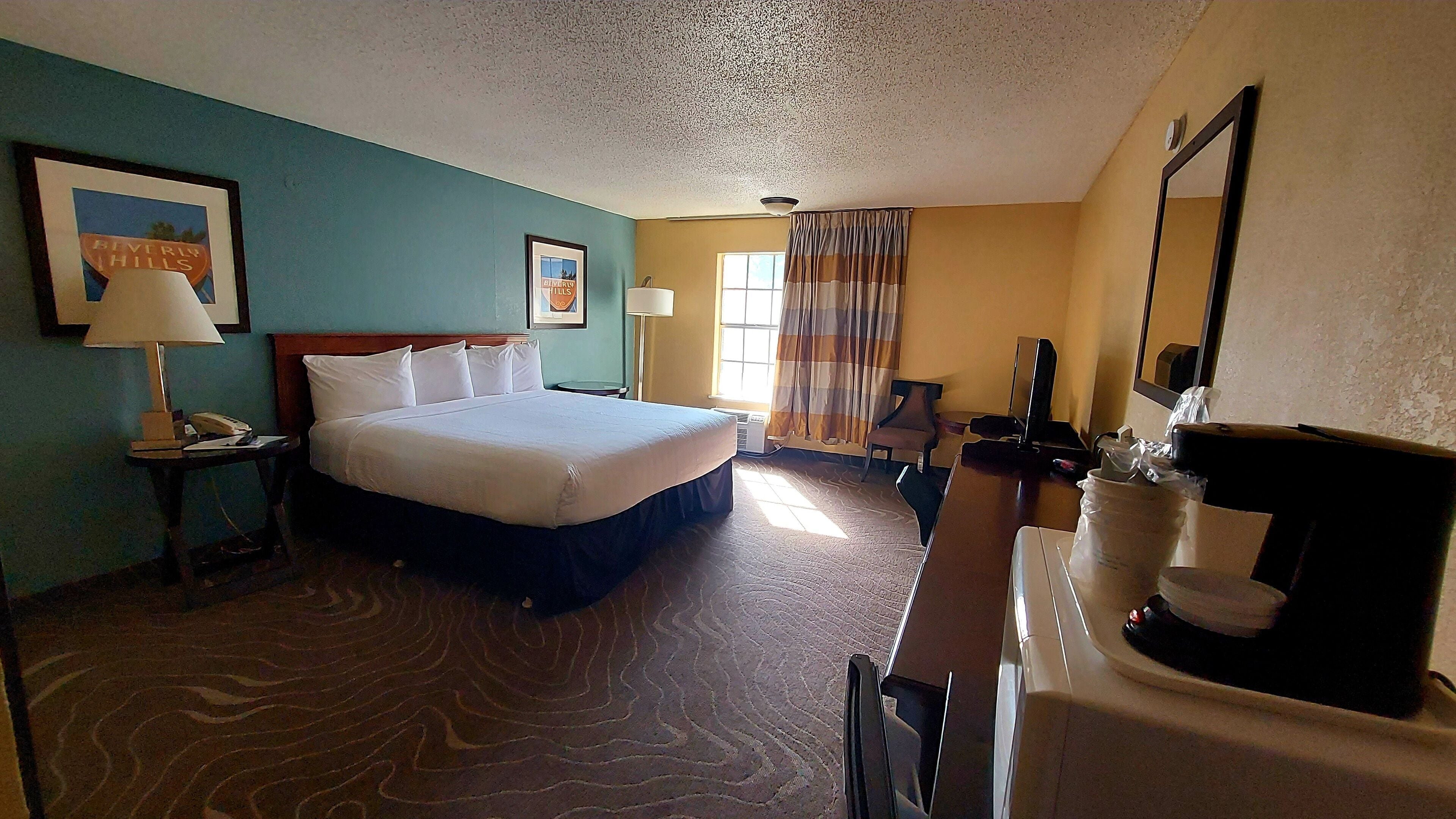 A hotel room with a bed, a desk, a chair, a TV, and a window with curtains.