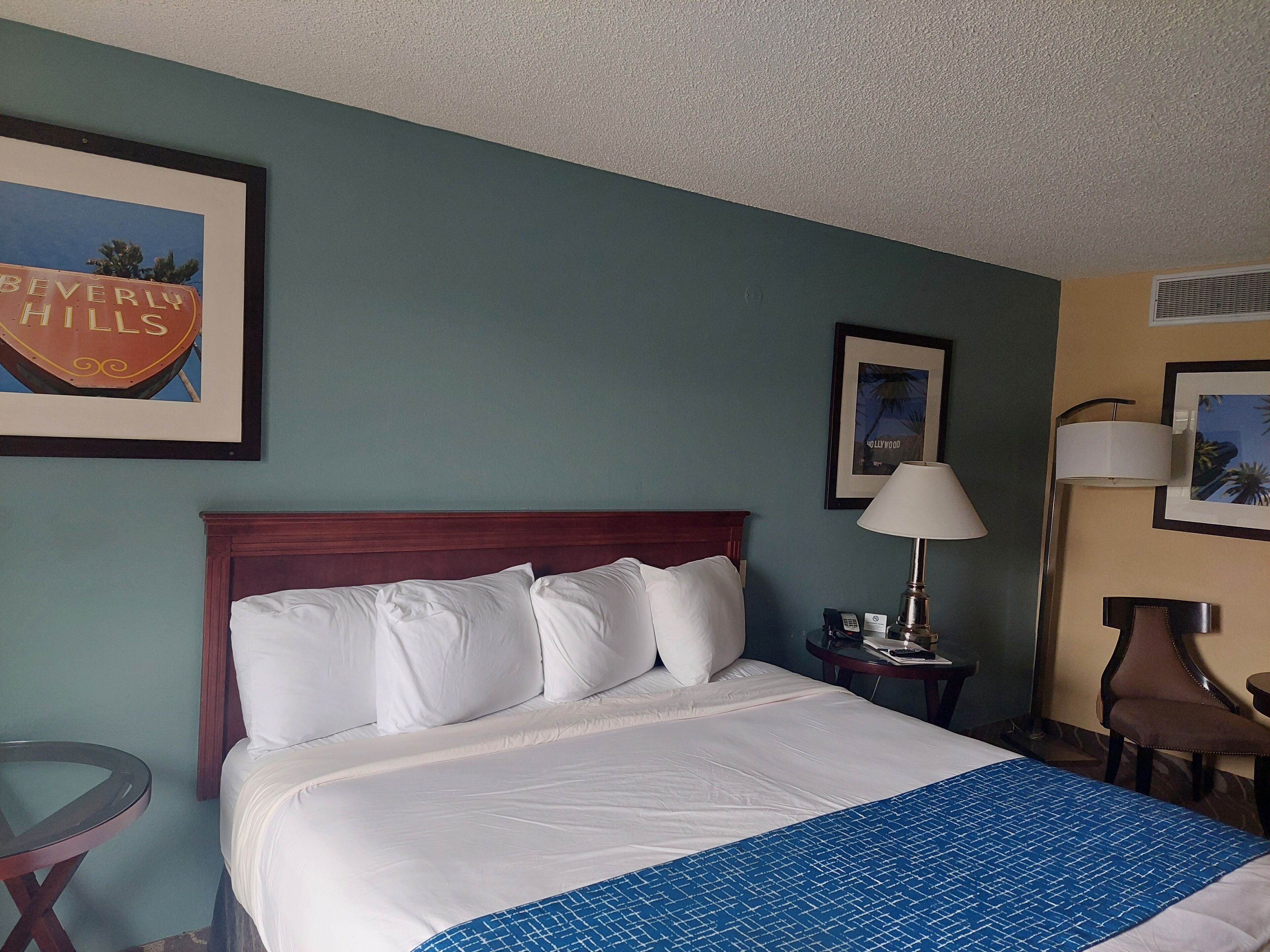 A hotel room with a bed, a nightstand, a lamp, and a chair.