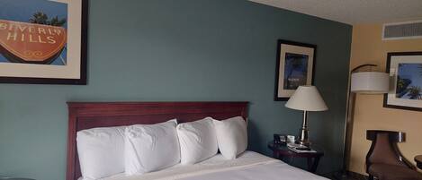 A hotel room with a bed, a nightstand, a lamp, and a chair.
