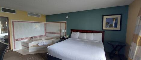 A hotel room with a large bed, a separate bathroom with a bathtub, a desk, and a chair.