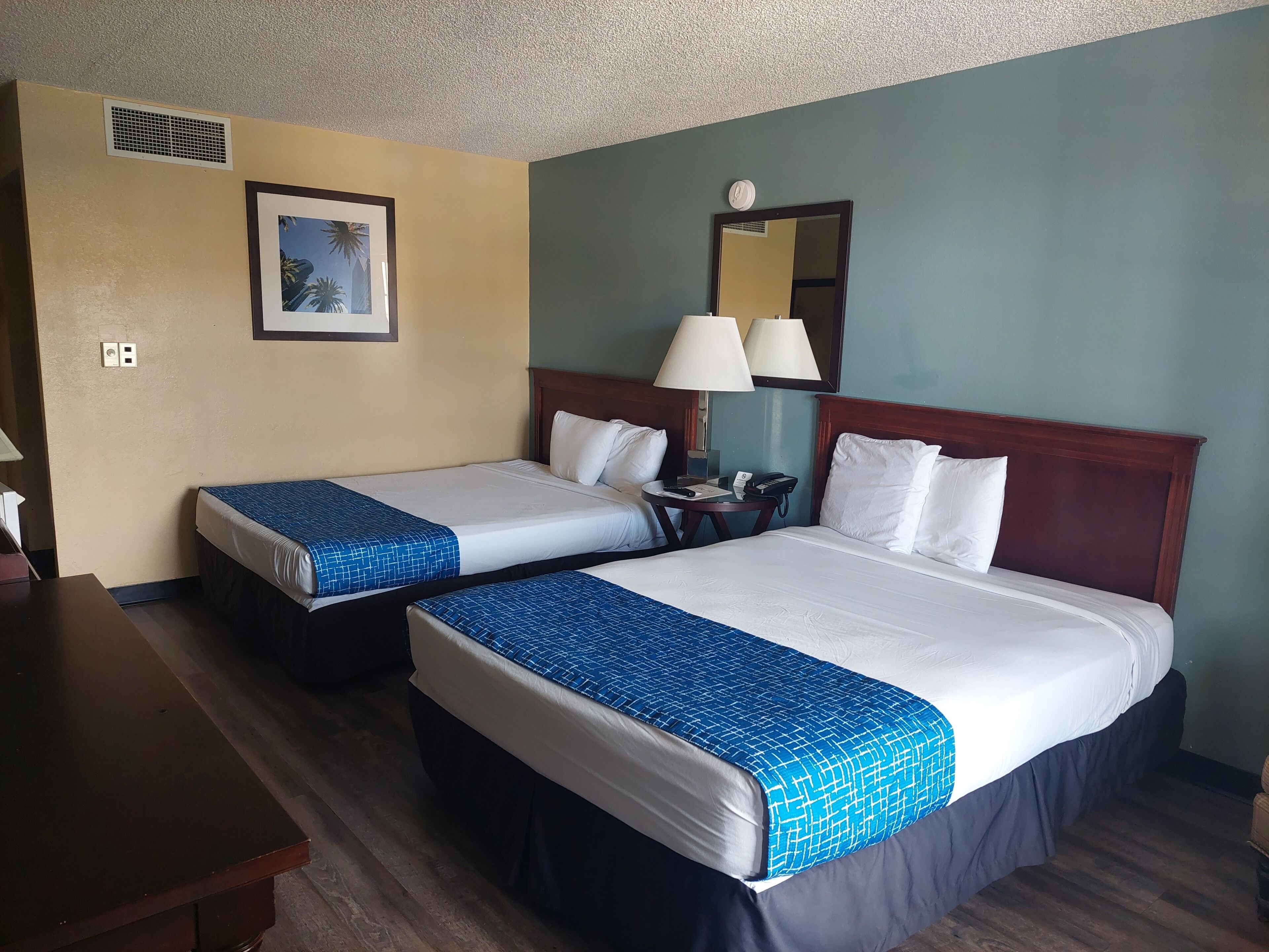 Habitación de hotel con dos camas, un escritorio, una lámpara y un cuadro en la pared.