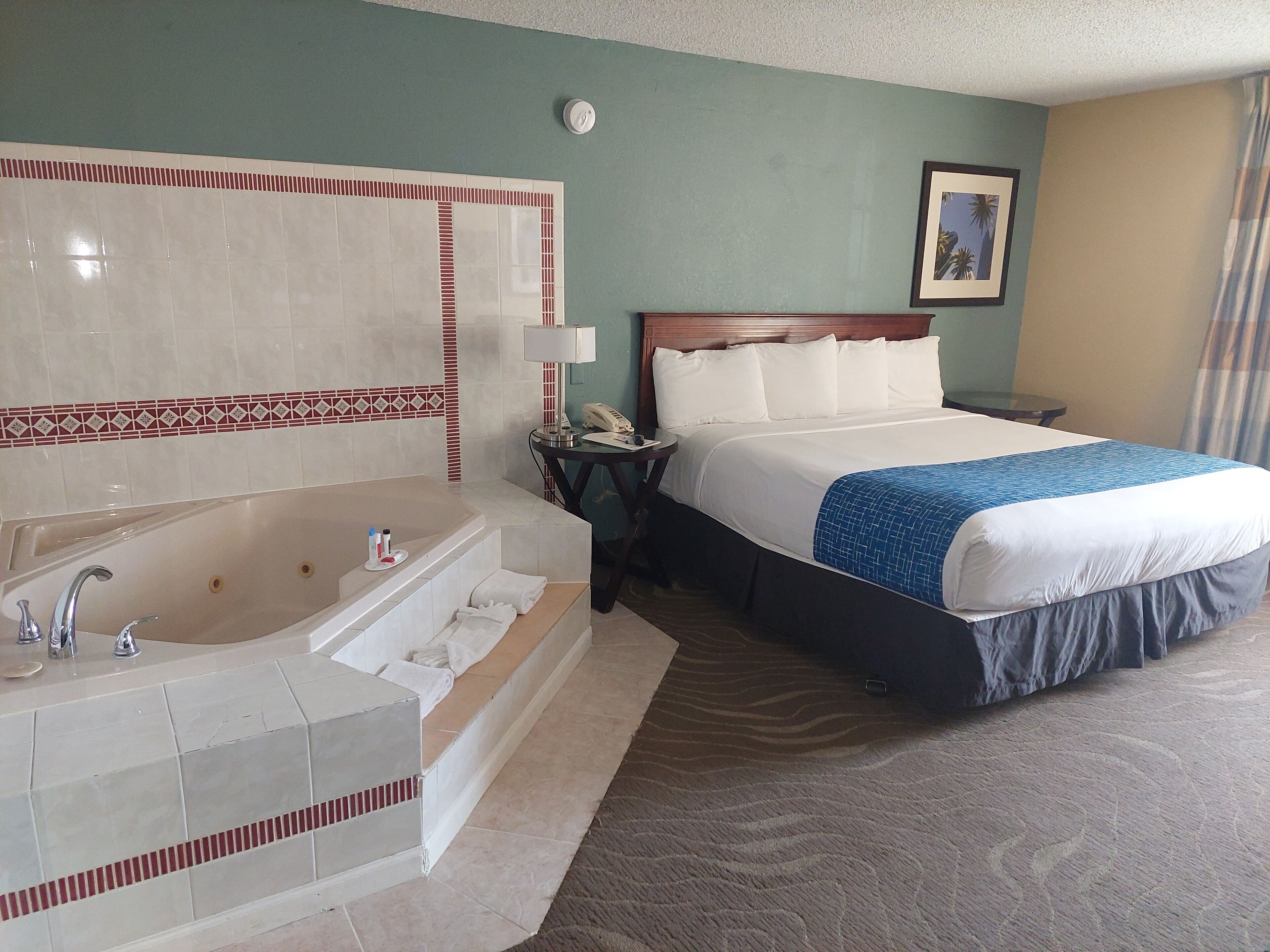 A hotel room with a large bed, a separate bathroom with a bathtub, and a small bedside table with a lamp.