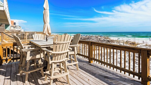 A wooden deck with a table and chairs, overlooking a beach with a wooden railing. - On the Beach, Big Deck, Chair Service, Steps onto the Sand (Miramar Beach)