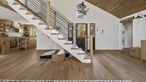 Eine geräumige Küche mit Holdekor, einer großen Kücheninsel, einer modernen Treppe mit einer Deckenleuchte und einem Blick ins Freie durch ein Fenster.