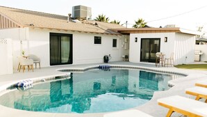 Une piscine à bord incurvé, entourée de chaises longues et d’un petit espace patio.