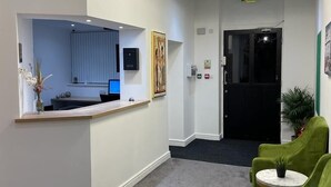 Un espace d’accueil avec un bureau, un tableau et un fauteuil vert.