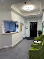 A reception area with a desk, a computer, a green chair, and a small table with a plant.