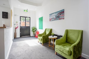 A reception area with a black door, two green armchairs, a small round table, a potted plant, and a framed picture on the wall.