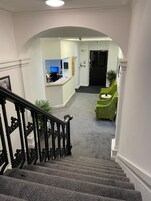 A staircase leading to a reception area with a desk and chairs, carpeted floors, and a door in the background.