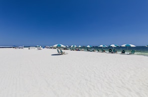 A beach with rows of green lounge chairs and blue umbrellas.