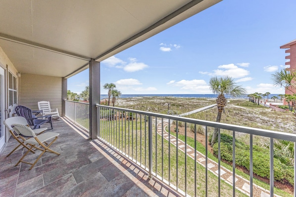 A balcony with a view of the beach and ocean, featuring a table and chairs.