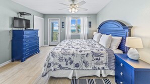 Un dormitorio con cama, ventilador de techo, televisor, cómoda y mesita de noche.