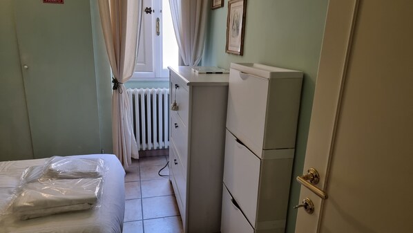 Una habitación pequeña y ordenada con una cama, un radiador, un tocador blanco y una puerta con un letrero que dice 'PRIVATE'.