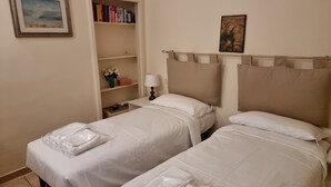 Habitación de hotel con dos camas, una estantería con libros, un cuadro y una mesita de noche con una lámpara.