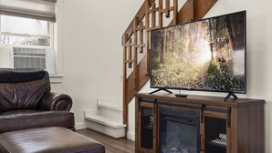 Un salon avec un canapé en cuir marron, un téléviseur à écran plat posé sur un meuble en bois et un escalier doté d’une rampe en bois.