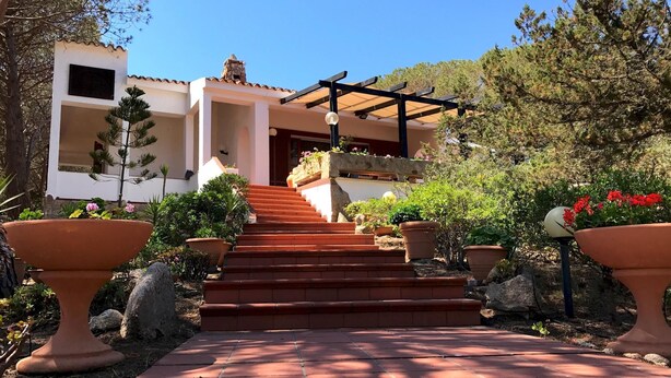A building with a stone facade, a wooden pergola, and a paved pathway leading to a set of stairs. - Villa La Maddalena in La Maddalena (La Maddalena)