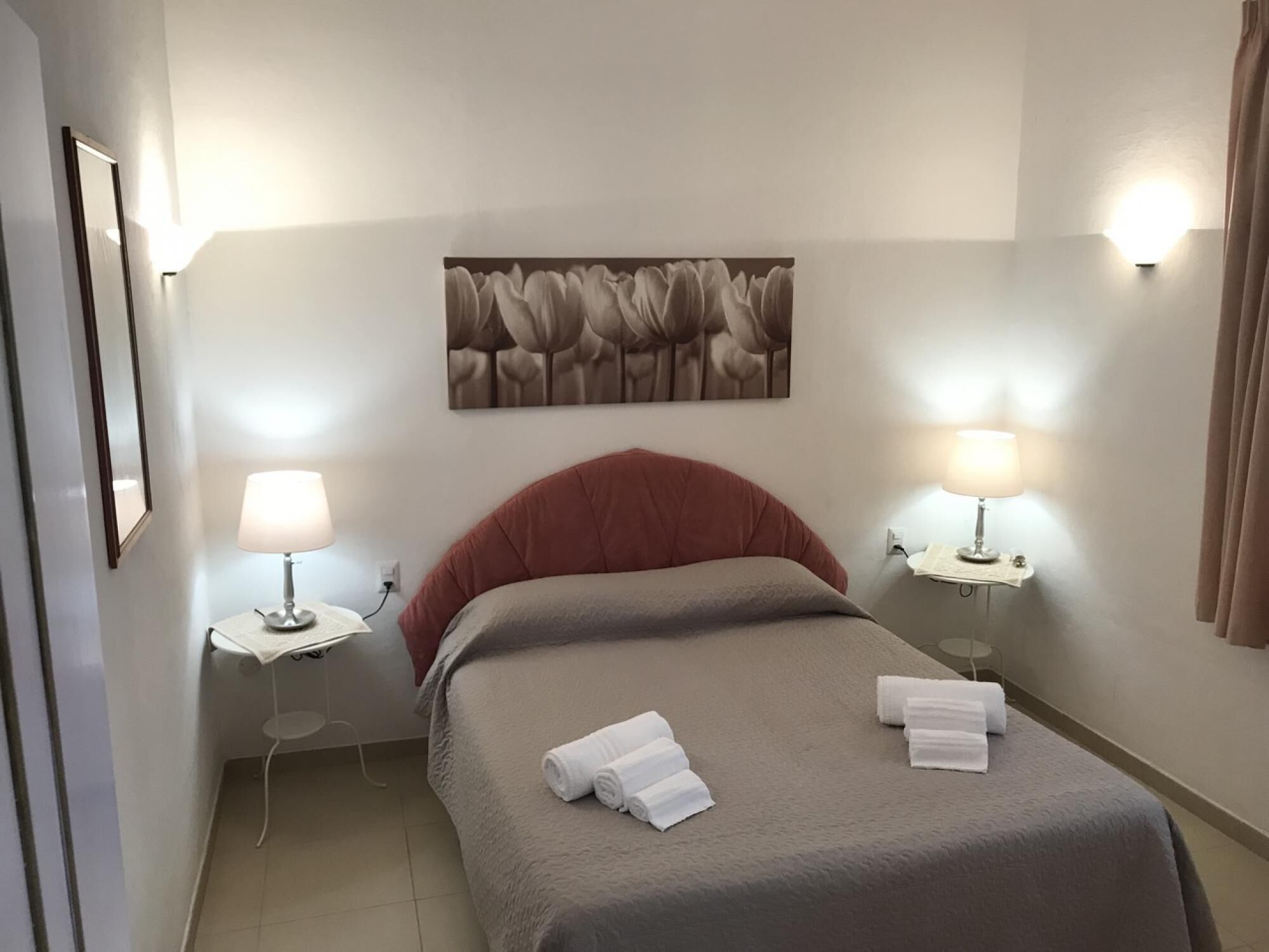 A hotel room with a bed, two bedside lamps, a wall-mounted picture, and a small table with a lamp.