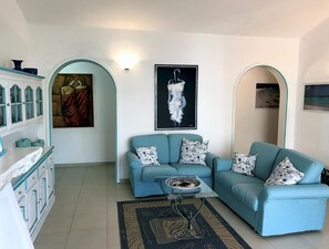 A living room with a blue sofa set, a coffee table, and a painting on the wall. - Villa La Maddalena in La Maddalena (La Maddalena)