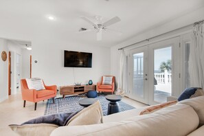 Una sala de estar moderna con un sofá, dos sillones, una mesa de centro y un televisor en la pared.