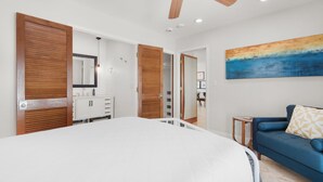 Une chambre avec un grand lit, un ventilateur de plafond, un tableau et un canapé bleu.