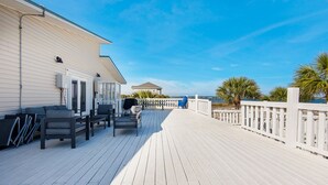 Une terrasse en bois avec des sièges d’extérieur, un bâtiment blanc et une vue sur l’océan.