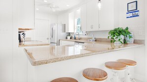 Une cuisine moderne avec des meubles blancs, un plan de travail en granit et des tabourets en bois.