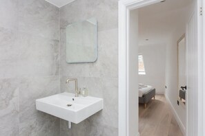 Un baño moderno con un lavamanos blanco, paredes de mármol y un espejo.