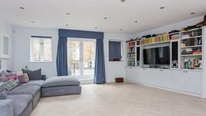 A modern living room with a grey sectional sofa, a flat-screen TV, and a white entertainment unit with books and decorative items.