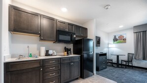 A modern kitchen with dark cabinetry, a black refrigerator, a microwave, and a coffee maker. There is a small dining area with a table and chairs. - Independence Stay (Houghton)