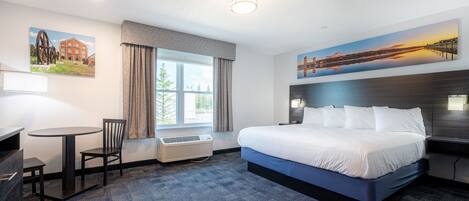 A hotel room with a large bed, a desk with a chair, a window with curtains, and artwork on the walls.