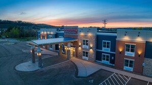 A hotel with a covered parking area, a sign for 'Independence Stay Hotel & Long-Term Suites', and a view of the surrounding landscape. - Independence Stay (Houghton)