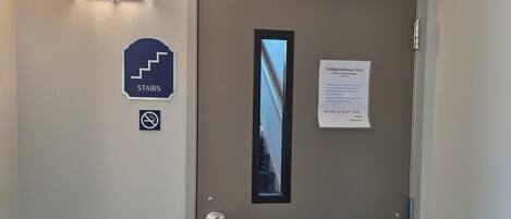 Entrada a una habitación de hotel con una puerta, un cartel que indica la ubicación de las escaleras, un letrero de 'no se admiten mascotas' y un aviso sobre la política de estancia independiente.