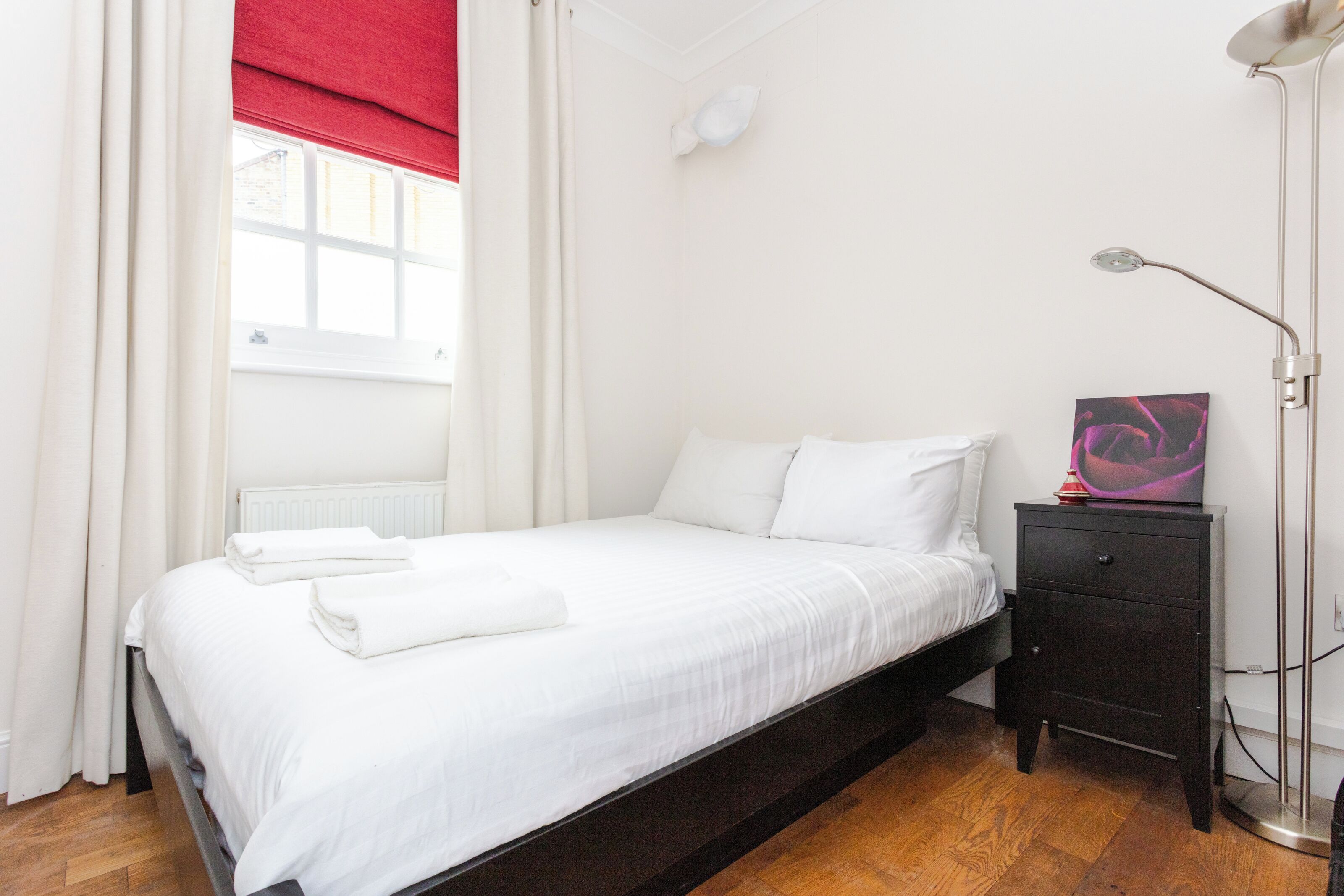 Un dormitorio con cama, mesita de noche, lámpara y ventana con cortinas.