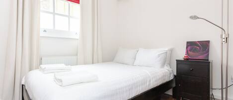 A bedroom with a bed, a nightstand, a lamp, and a window with curtains.