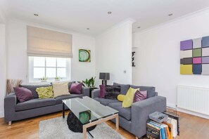 A modern living room with two grey sofas, a glass coffee table, and a bookshelf.