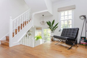 A spacious room with a wooden staircase, a black leather chair, a large window, and a potted plant.