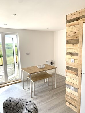 A modern kitchen with a wooden table, bench, and a decorative white bowl. - Countryside lodge 5 minutes from beach (St Merryn)