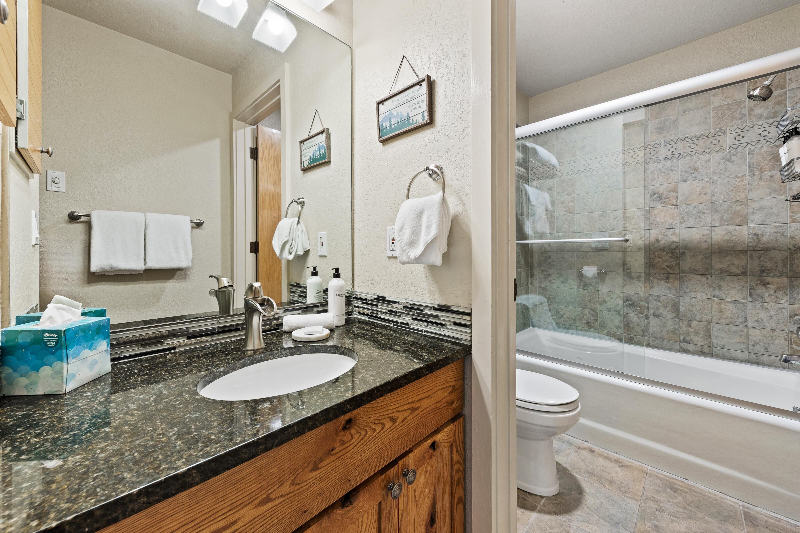 A bathroom with a granite countertop, a sink, a mirror, a toilet, and a glass-enclosed shower.