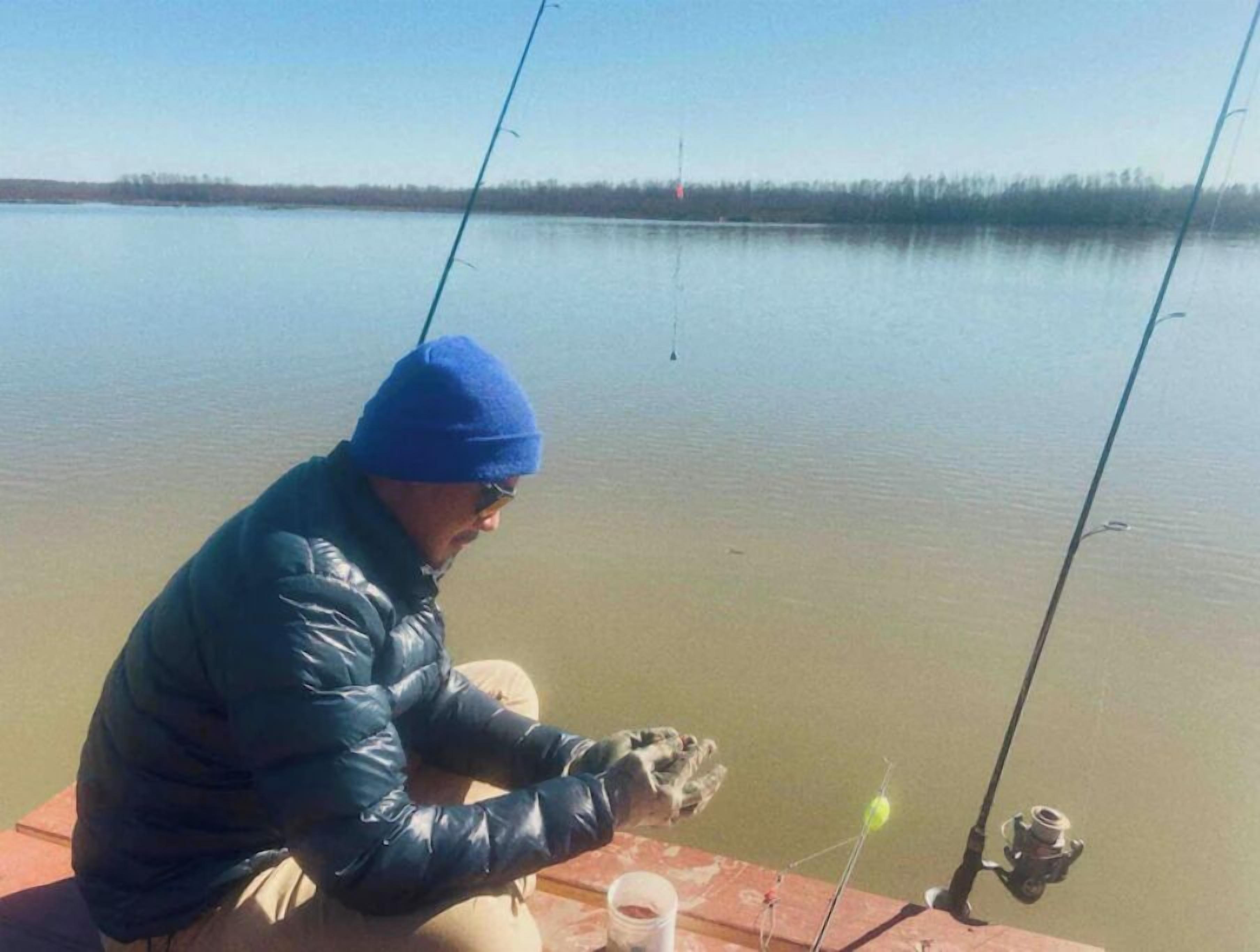A person sitting on a dock by a calm lake, holding a fishing rod.