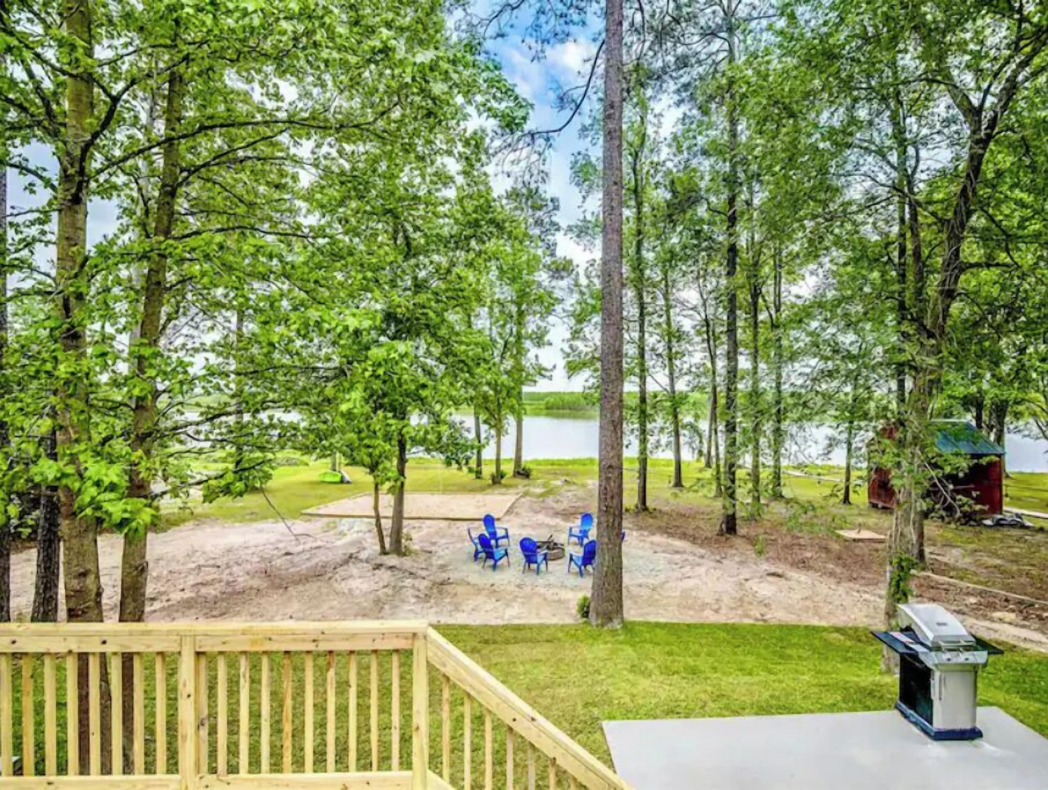 A deck with a grill and outdoor seating area overlooking a lake, surrounded by trees.