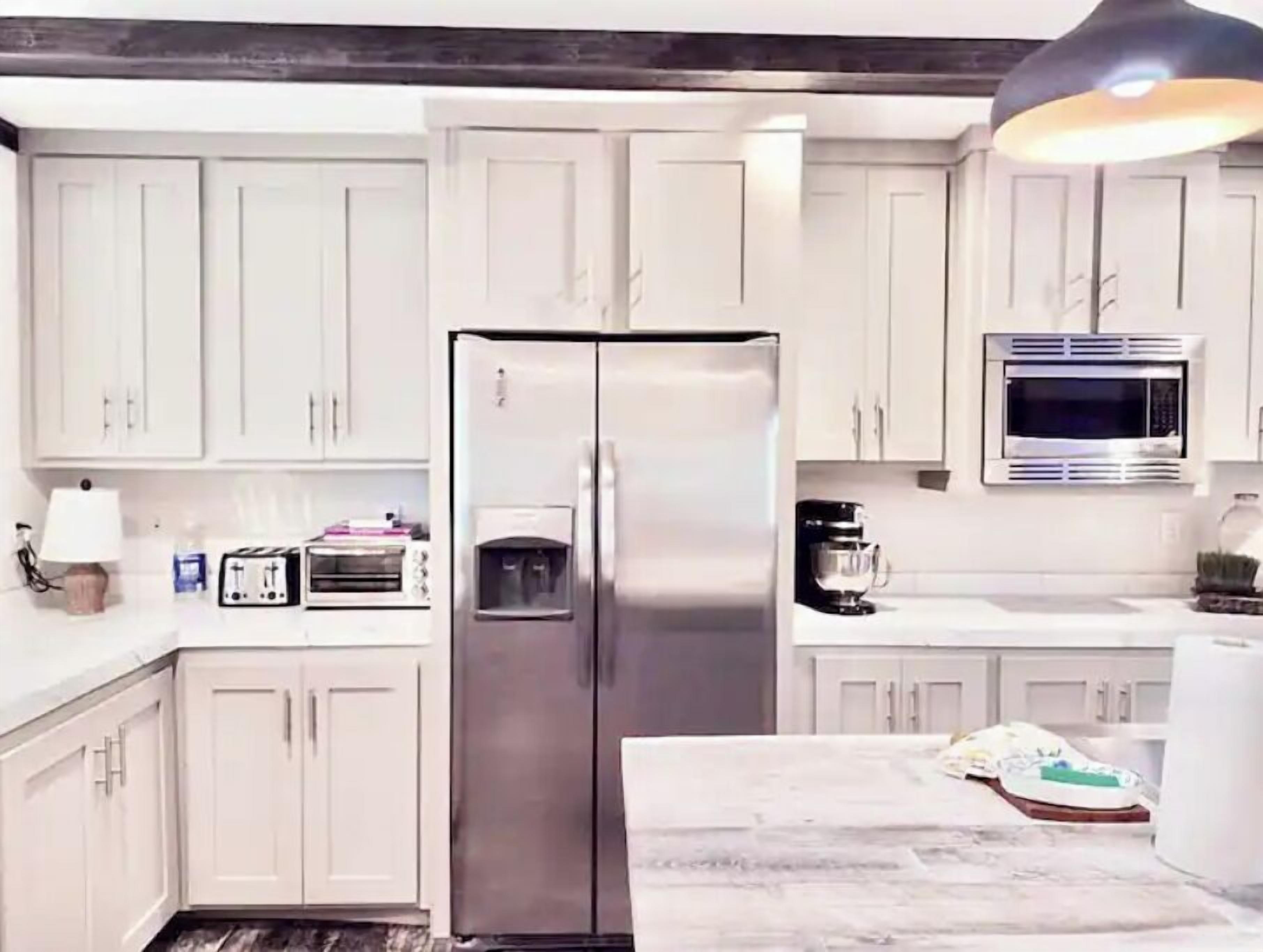 Una cocina moderna con gabinetes blancos, un refrigerador de acero inoxidable, un microondas y una cafetera.