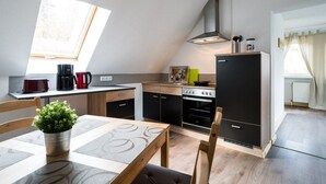 A modern kitchen with a skylight, a dining area with a table and chairs, and a black refrigerator. - Landhotel Prälank (Neustrelitz)